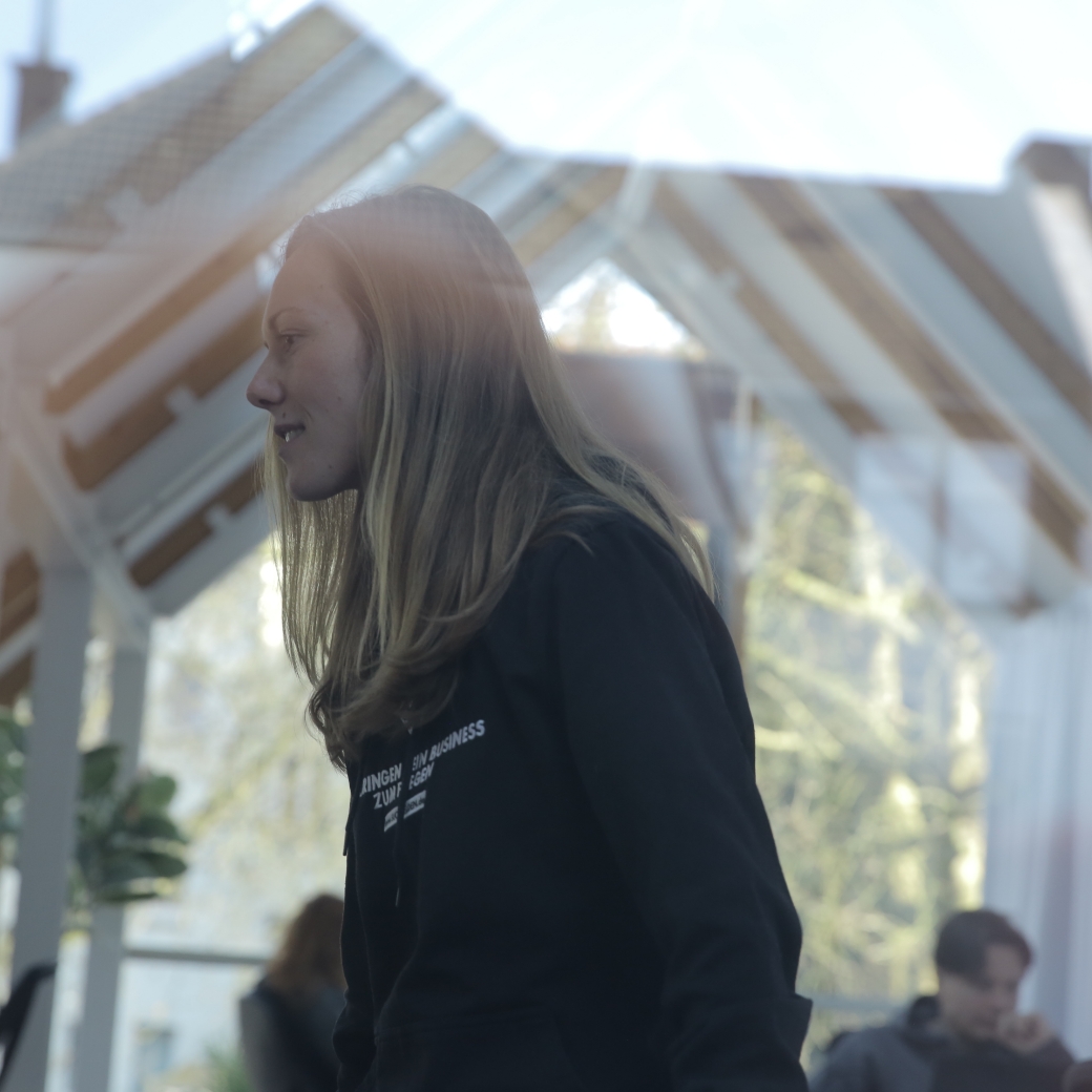 Frau steht lächelnd in lichtdurchflutetem, modernem, glasüberdachtem Büro