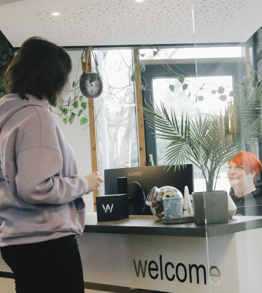 Empfangsbereich: Person steht am Empfangsschalter und spricht mit Mitarbeiterin