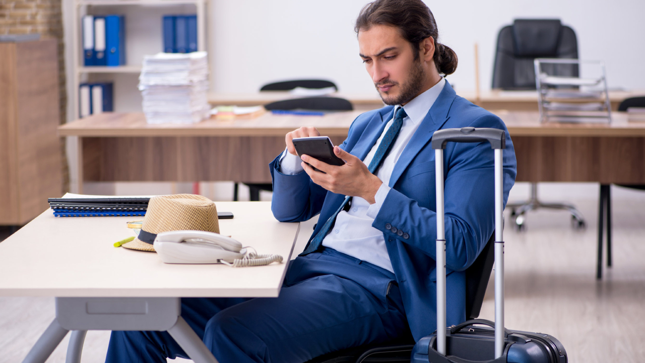 Lohnabrechnung Düsseldorf: Mann im Anzug sitzt mit Handy im Büro und arbeitet