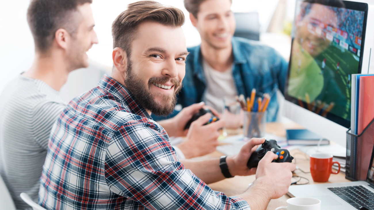 Lohnabrechnung Frankfurt: Mann, lächelnd, hält Controller, spielt Videospiel am Schreibtisch