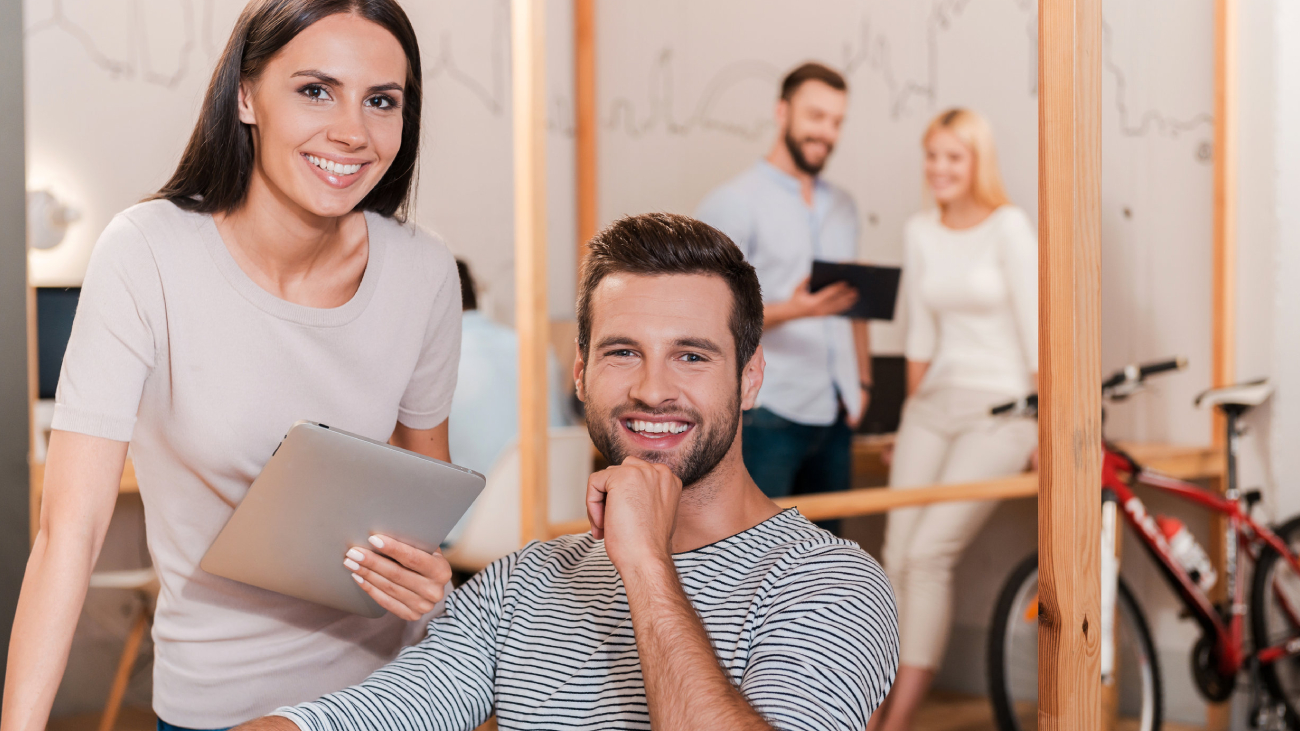 Lohnabrechnung Frankfurt: Person mit Tablet lächelt, andere arbeiten im Bürohintergrund