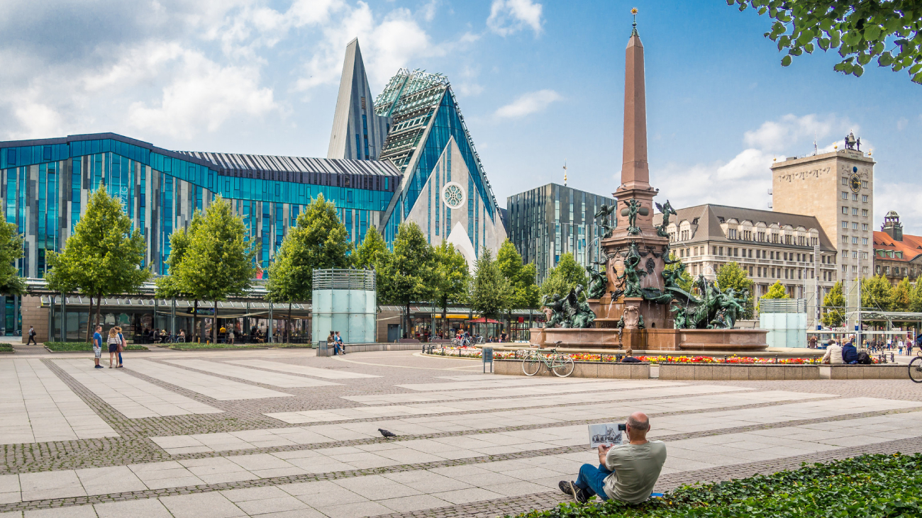 Lohnabrechnung Leipzig: Mann liest Zeitung auf Platz vor modernen Gebäuden, Leipzig