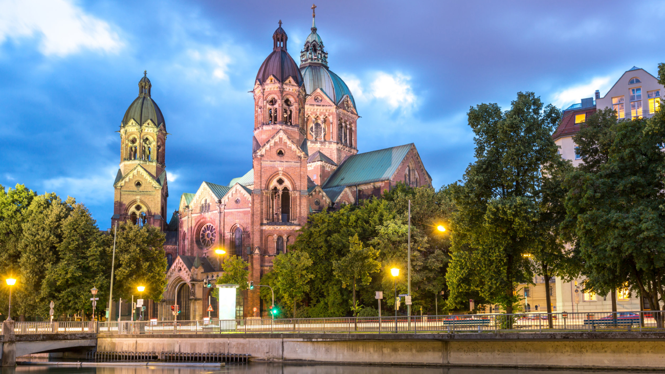 Lohnabrechnung München: Kirche leuchtet abends, umgeben von Bäumen und beleuchteten Straßen